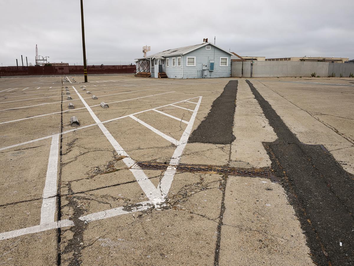 Concrete parking lot with guidelines and asphalt stripes leading in different directions, with naval building in background