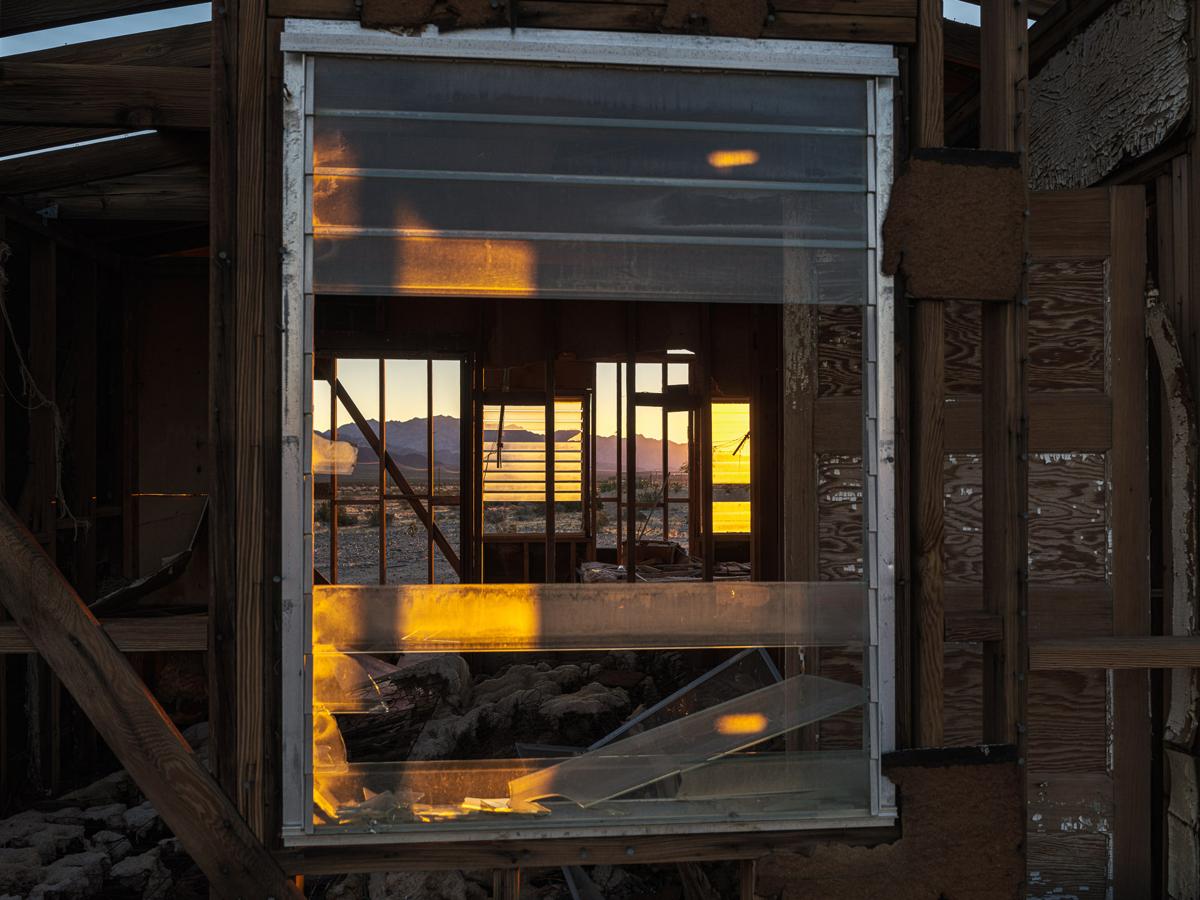 Sunrise seen through broken louvred windows at front and back of abandoned house.