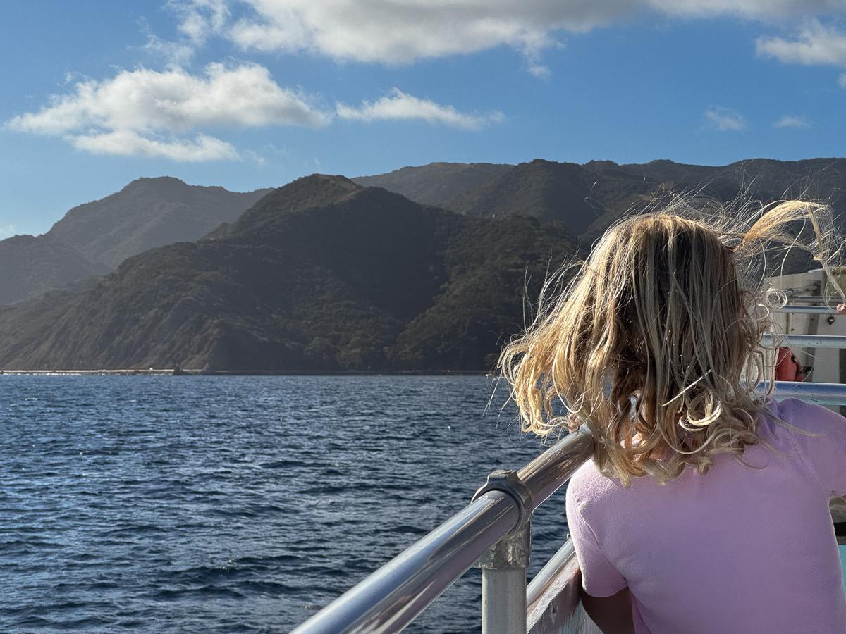On boat approaching island, girl with windblown hair has back to camera.