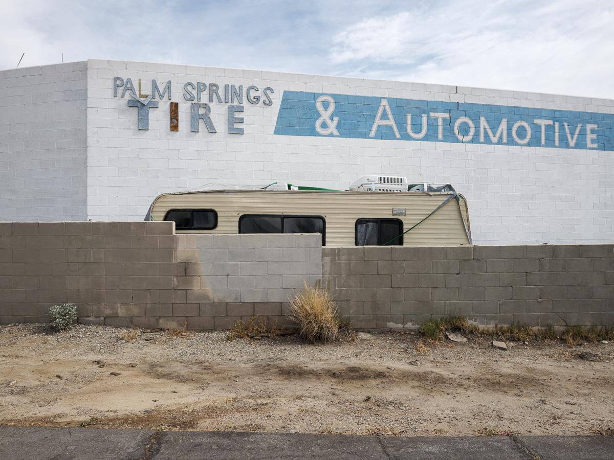 Top of a recreational trailer seen over a newly patched cinderblock wall in front of the rear wall of Palm Springs Tire & Automotive.