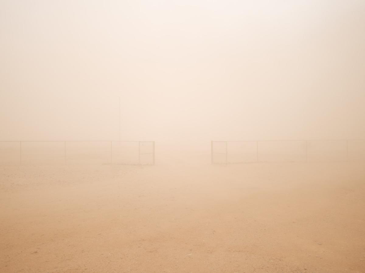 Chain-link fence barely visible through dense sandstorm.