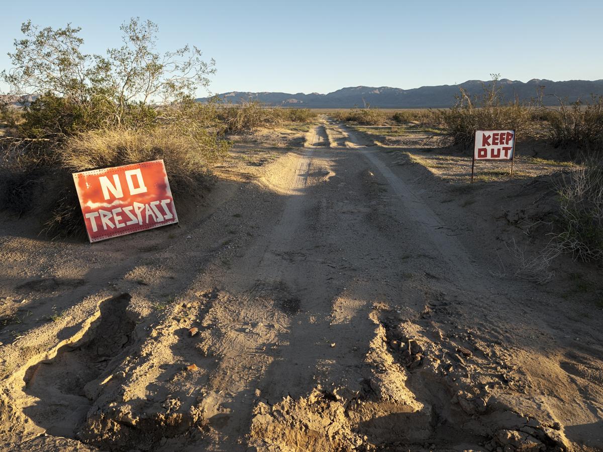 A dirt road leads toward distant mountains in desert landscape, with 