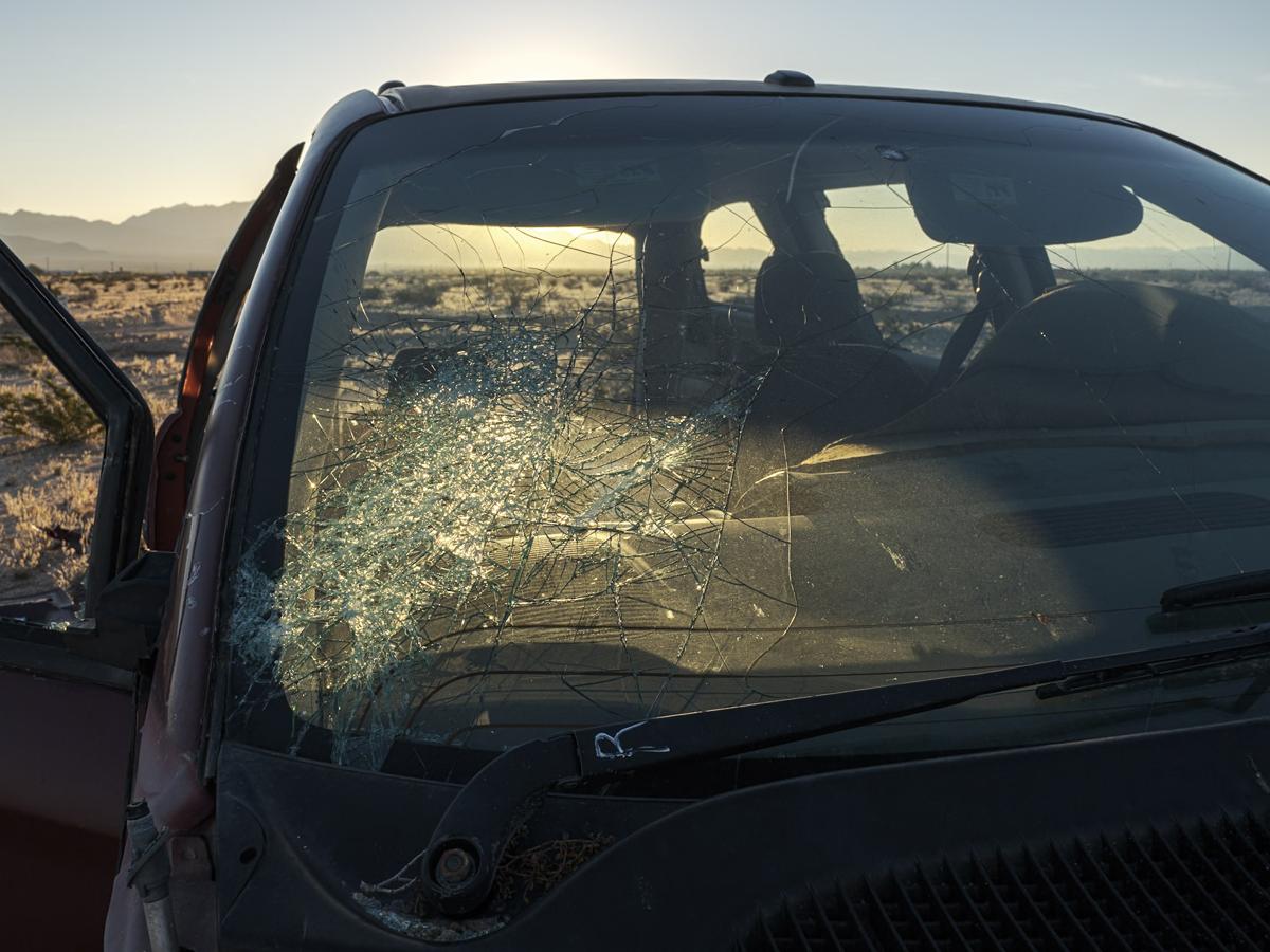 The heavily cracked windshield of an minivan abandoned in the desert is lit from behind by sunrise.