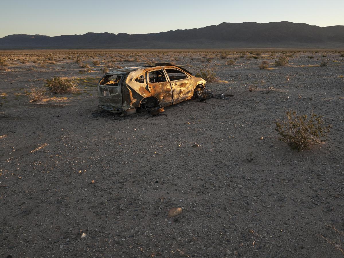 Burnt shell of abandoned car in desert landscape.
