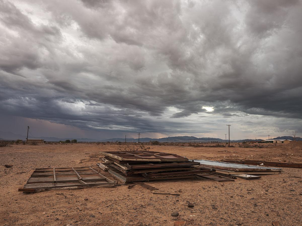 Multicolored rain clouds over pile of debris in desert landscape.