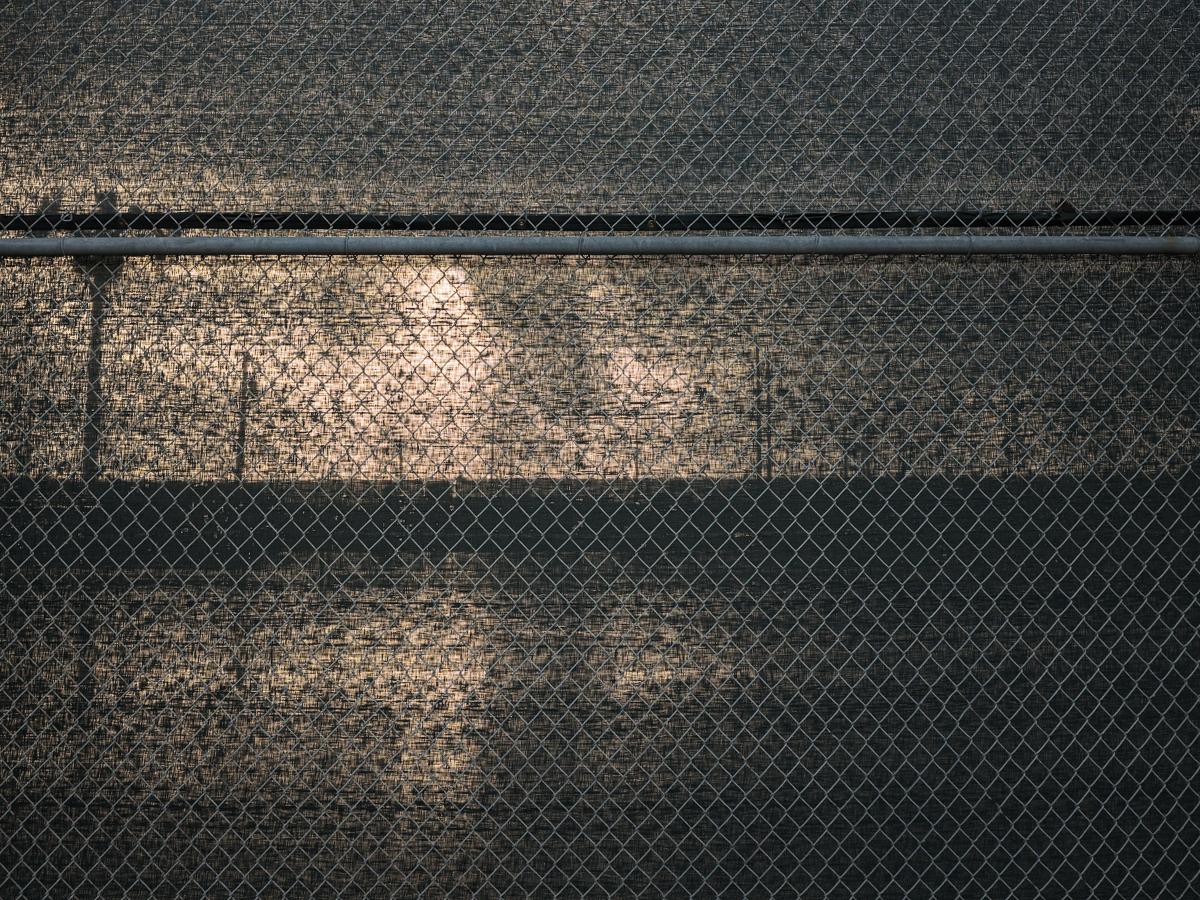 Sun and power-line shadows dimly visible behind chain-link fence with netting.