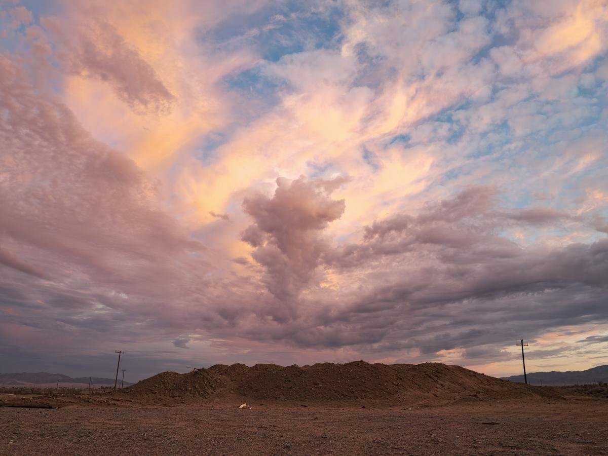 Dramatic sunset cloud formation over pile of dirt flanked by distant power poles.
