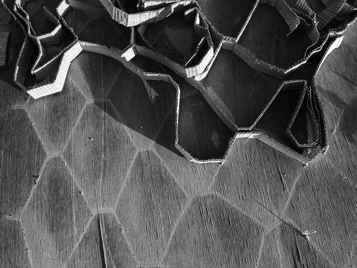 Coiled strip of narrow cardboard resting on plywood board with hexagonal markings.
