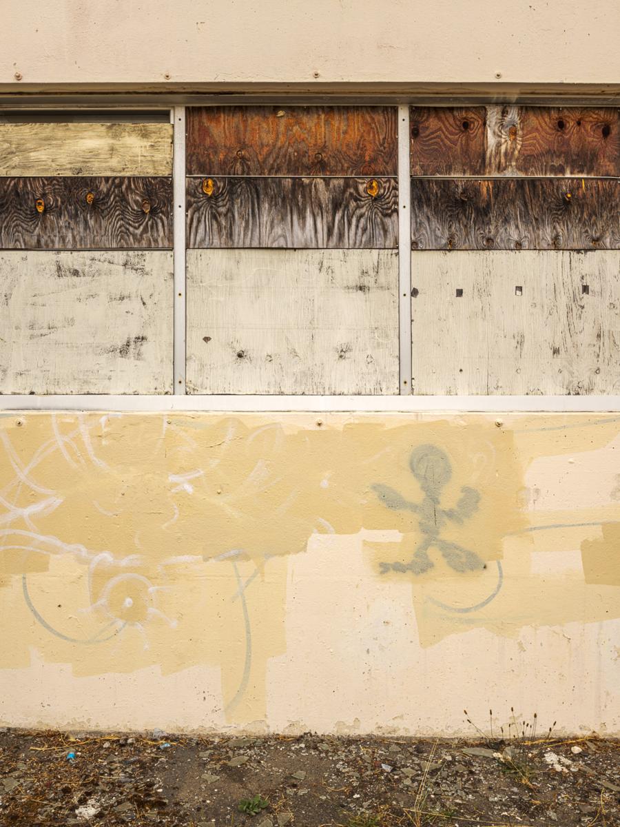 Dilapidated wall with boarded-up windows, layers of roller paint, and a blobby human-shaped graffito.