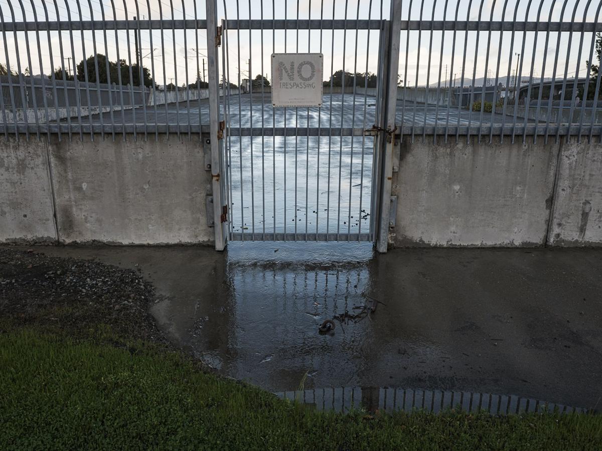 A locked gate with No Trespassing sign guarding empty concrete plaza.