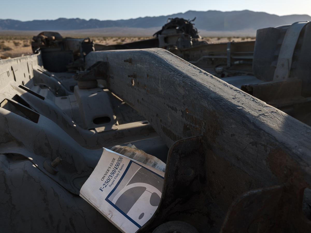 An F-250 owner's guide sits atop an overturned truck in desert landscape.