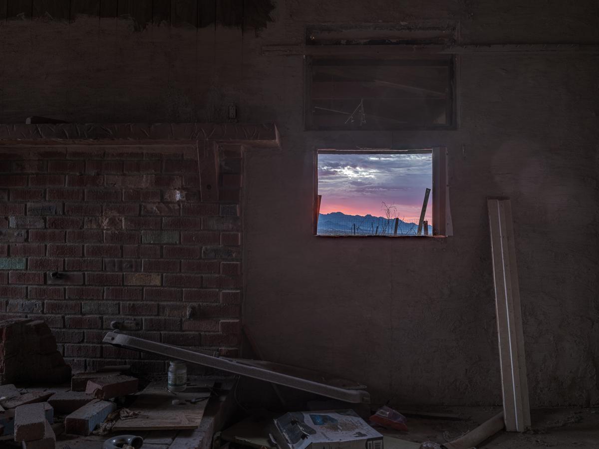 Interior of abandoned house with mountains and predawn sky showing through unglazed window.