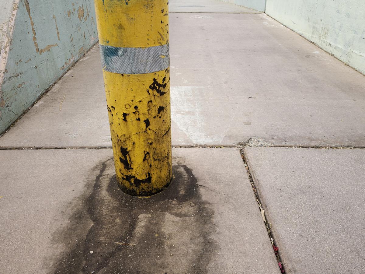 A weathered yellow post stands in front of a grid of pastel-colored concrete slabs.
