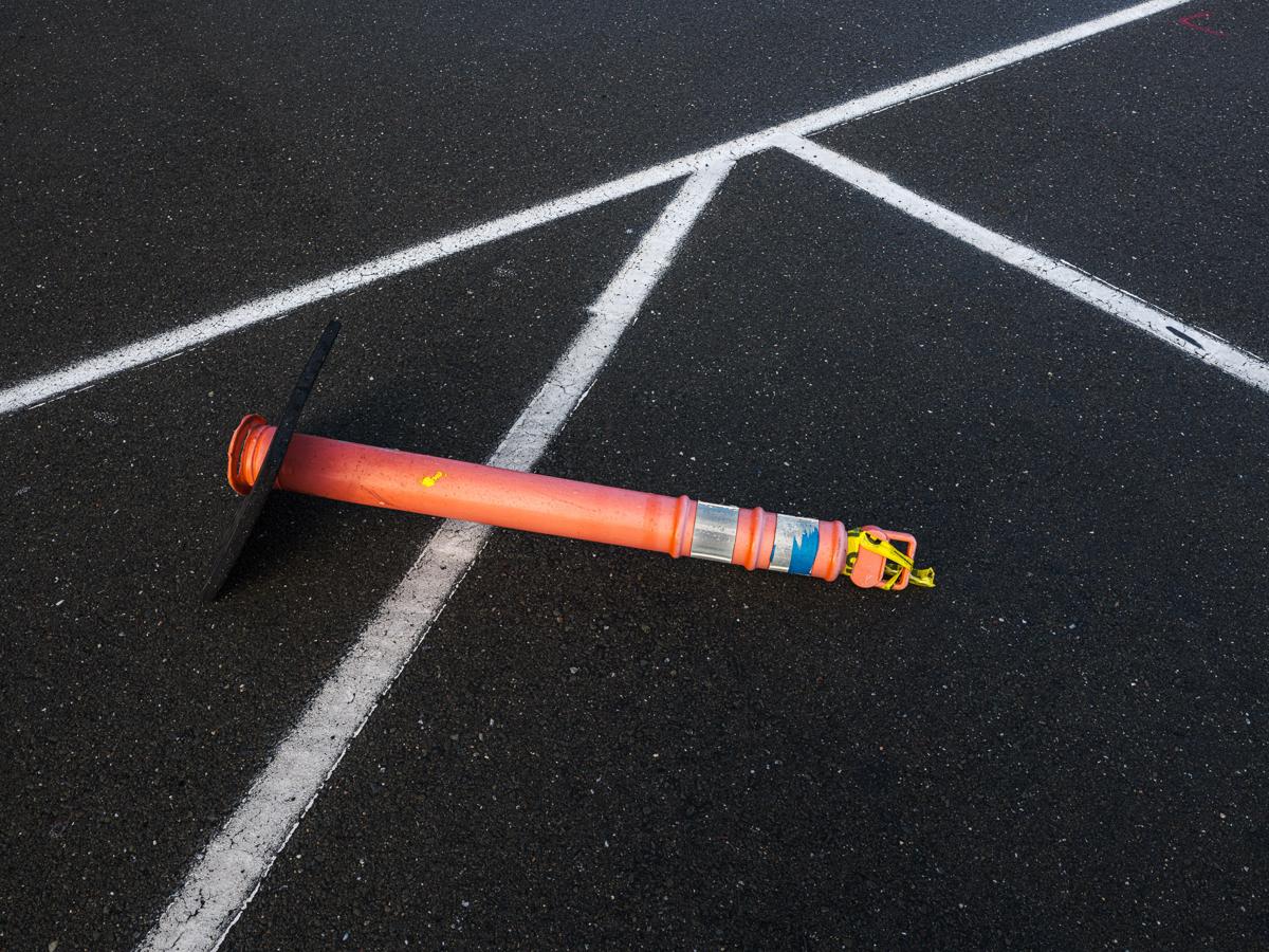 An orange traffic pylon lies across a sharply angled pattern of parking space lines.