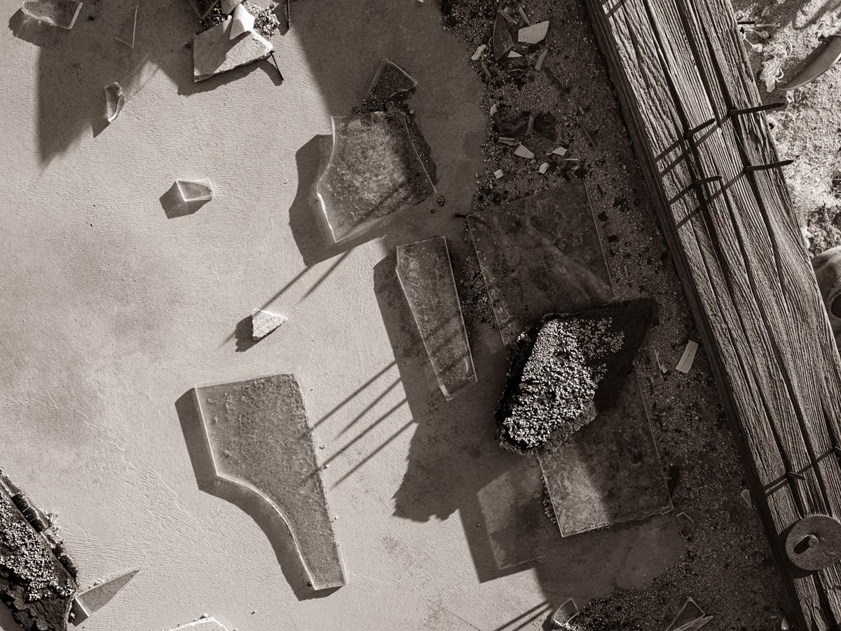 Shards of glass, asphalt, and wood lie on concrete pad in desert sand, lit by sunrise.