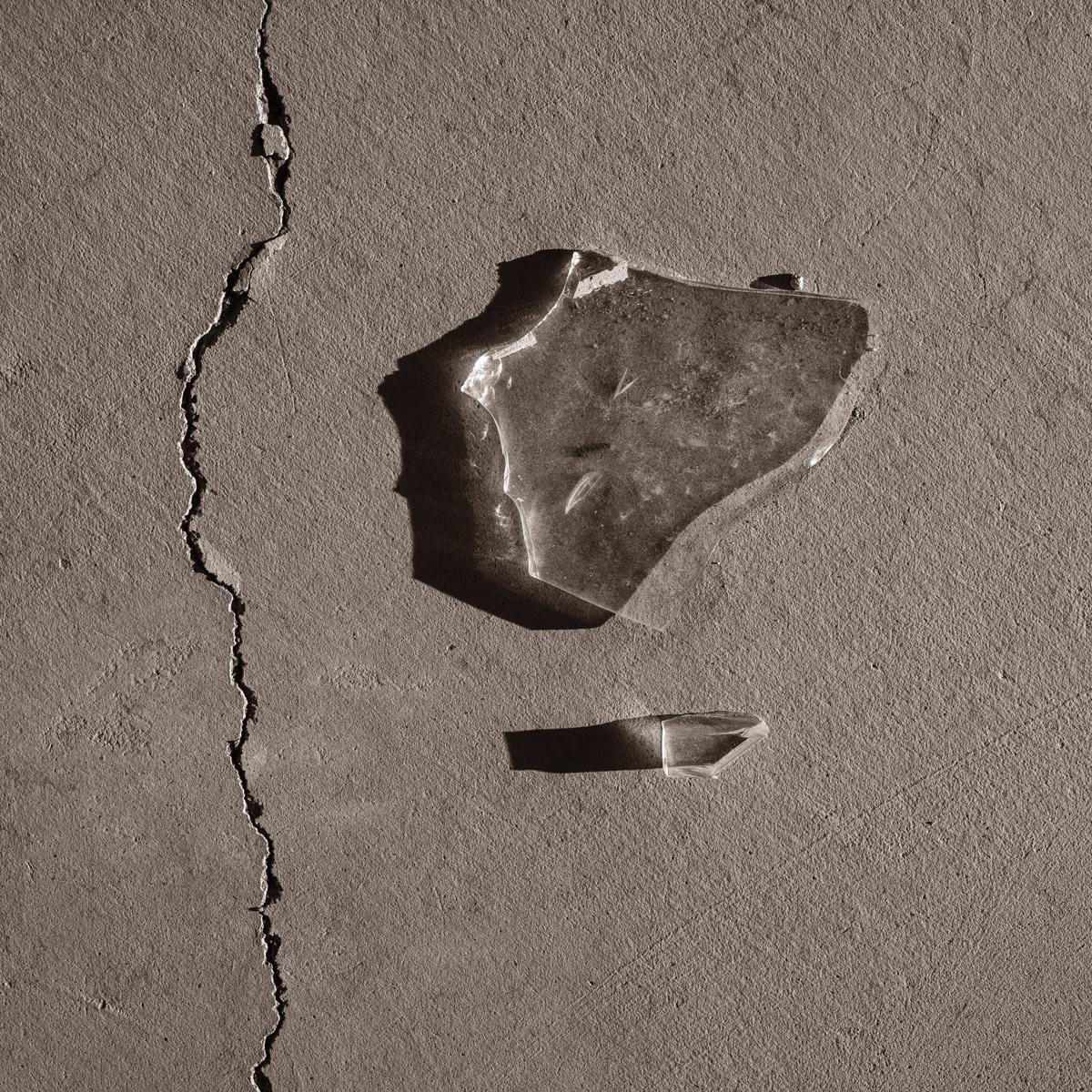 Shards of broken glass lying on cracked concrete floor, lit by rising sun.