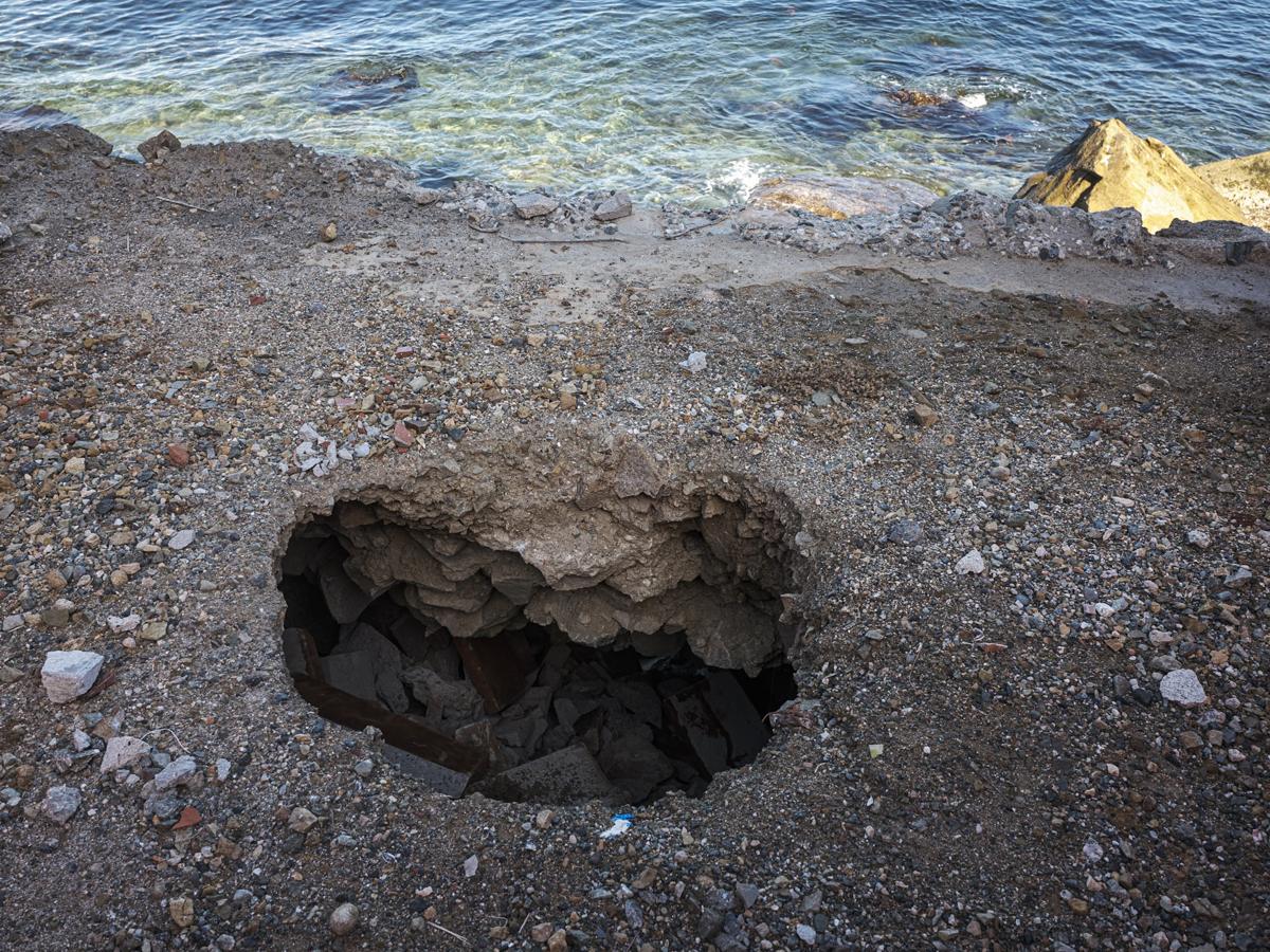 Sinkhole in shady foreground with sunlit sea and rocks in background, seemingly on the same plane.
