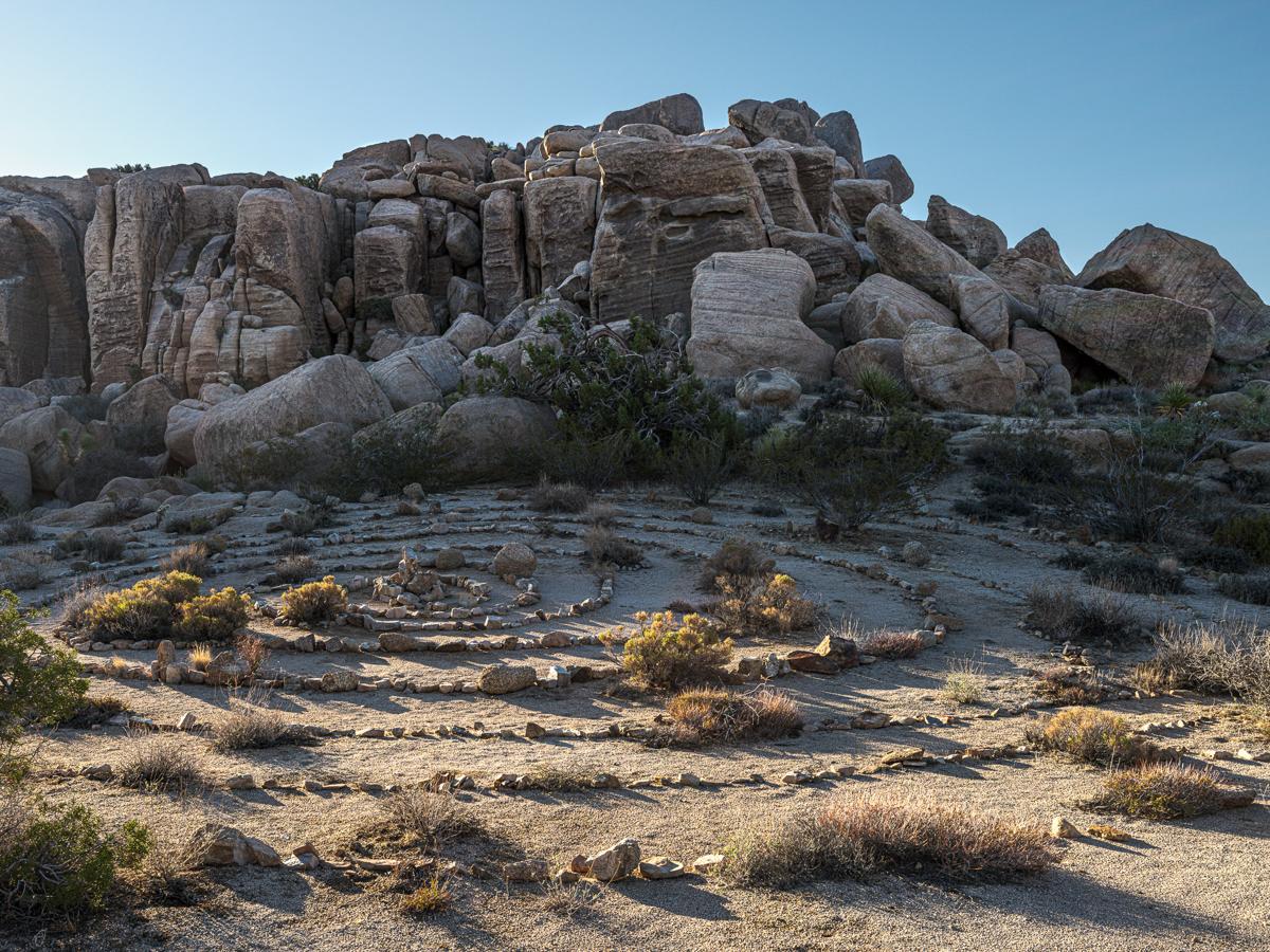 A spiral labyrinth made of found rocks, with a cairn in the center, against a cliff of jumbled rocks.