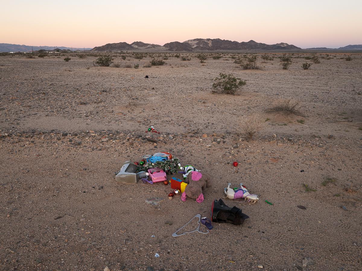 A pile of brightly colored discarded toys in desert landscape with moutain in background.